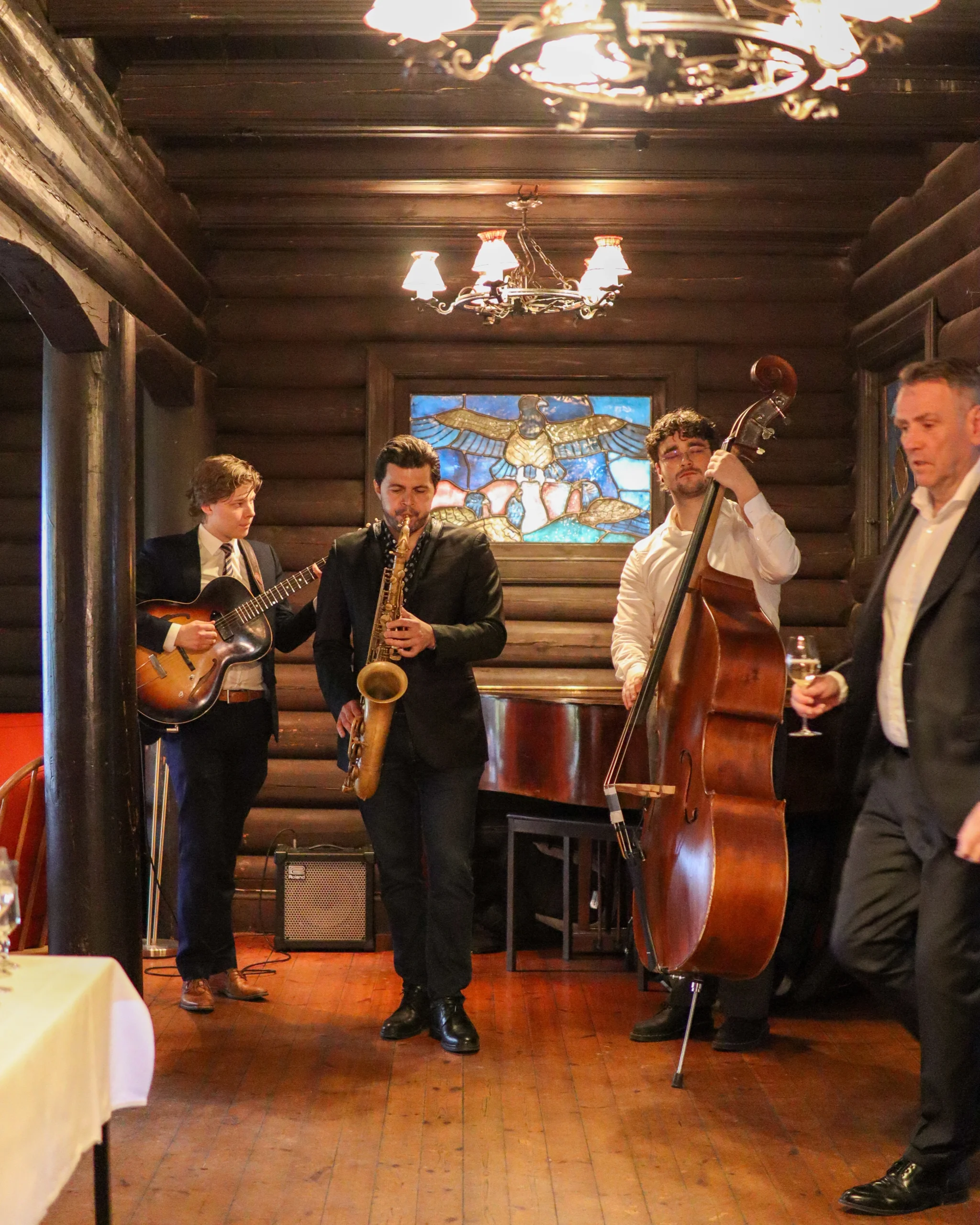 Cool jazz band performing at a private indoor event, featuring saxophone, contrabass, and guitar