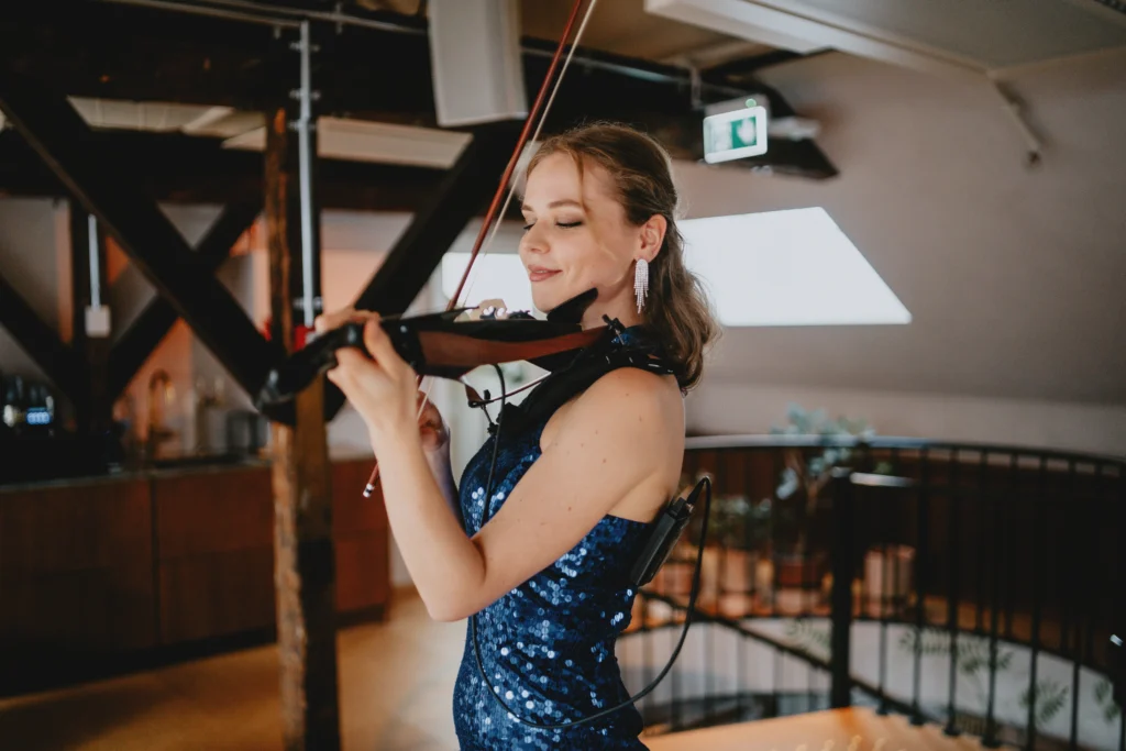 Female violinist in a blue sequined dress performing at a romantic event indoors, with soft lighting and elegant decor in the background.