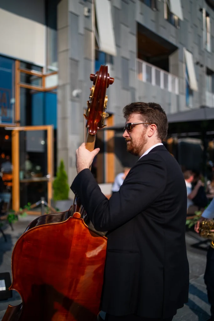 En jazzkontrabassist som opptrer utendørs i dress, med byomgivelser i bakgrunnen.